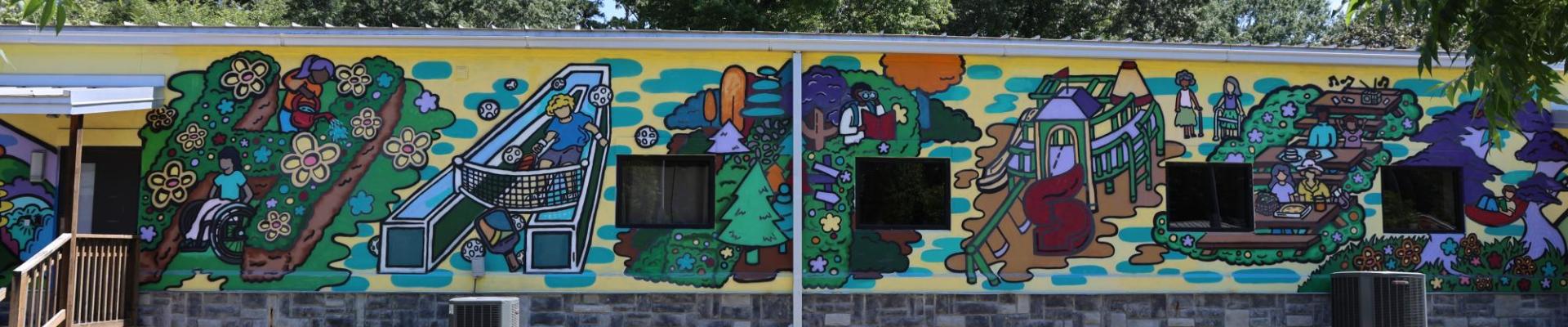 Mural on the back of a building showing people being active in a park.
